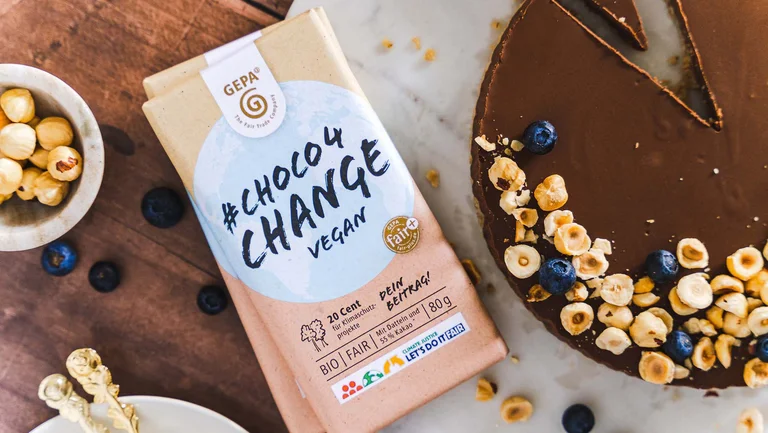 Schokotarte von oben mit Nüssen darauf, daneben zwei Packungen vegane Dattelschokolade