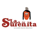 Logo: Auf wei&szlig;em Hintergrund ist eine Cashewfrucht mit Gesicht und langen schwarzen Haarz&ouml;pfen zu sehen. Dazu die Schrift: "La Sure&ntilde;ita. Un sue&ntilde;o hecho realidad"