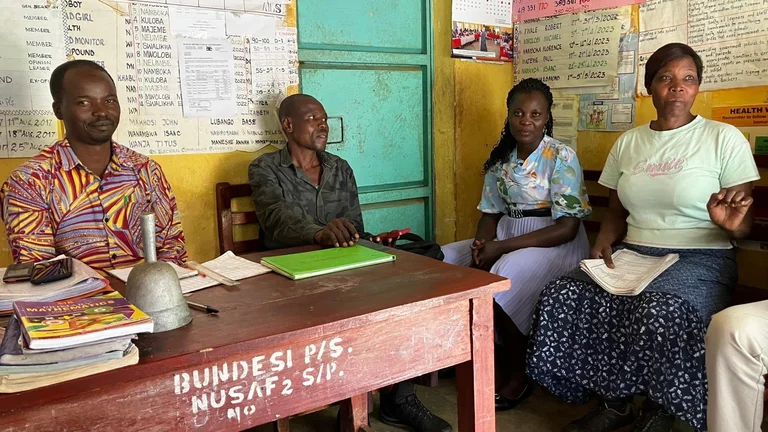 Vier Personen sitzen in einem Raum mit Schreibtisch, um sie herum an den W&auml;nden handgeschriebene Poster.