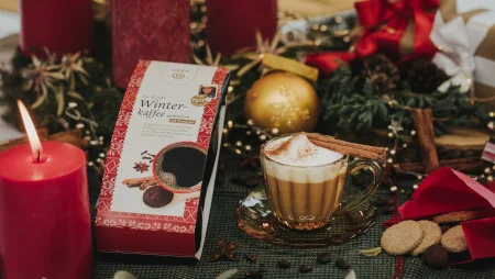 Auf einem weihnachtlich dekorierten Tisch mit Tannenzweigen, Christbaumkugeln und Kerzen steht eine Tasse Kaffee und eine Packung GEPA-Winterkaffee