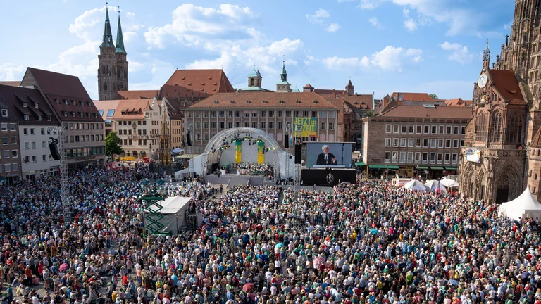 Blick auf den N&uuml;rnberger Hauptmarkt w&auml;hrend des Er&ouml;ffnungsgottesdienstes des Kirchentags 2023. Vor einer B&uuml;hne sitzen viele Hundert Menschen.