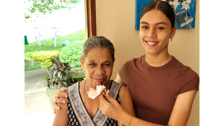 Enkeltochter (16) hält ihrer Großmutter einen Schokoriegel vor den Mund