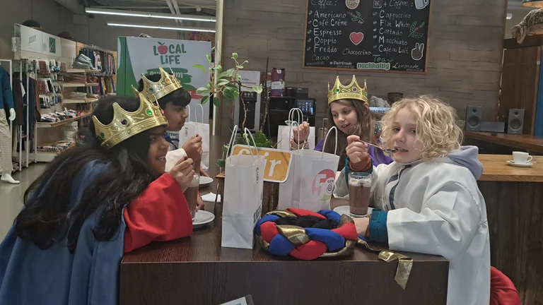 Vier Sternsinger-Kinder (zwei Jungs, zwei M&auml;dchen) sitzen an einer Theke und trinken Kakao.