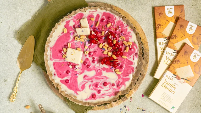Wei&szlig;-pinke Tarte von oben. Daneben 3 Packungen helle GEPA-Schokolade