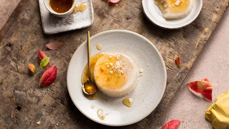 Panna Cotta mit Löffel auf einem Teller, verziert rotem Laub auf der Tischplatte