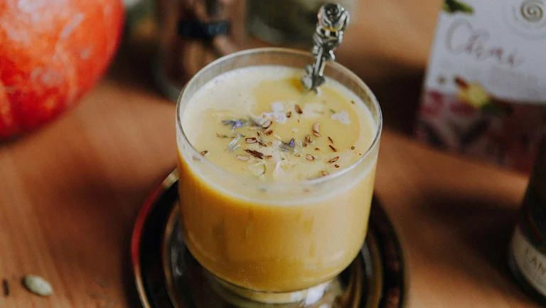 Glasbecher mit Kürbis-Chai-Latte, aus dem ein Löffel guckt