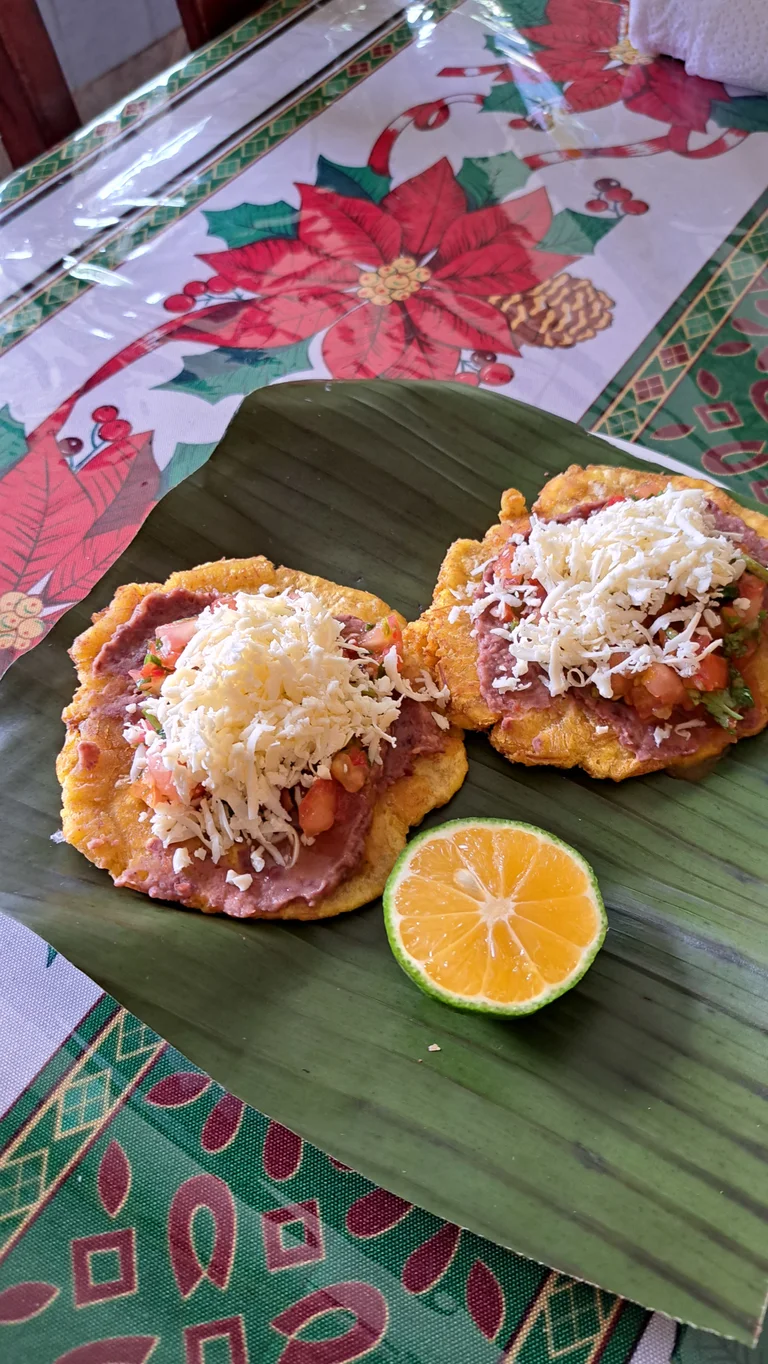 "Patacones", gebackene Kochbananenscheiben, auf einem Bananenblatt serviert, auf einer Tischdecke mit Blumenmuster