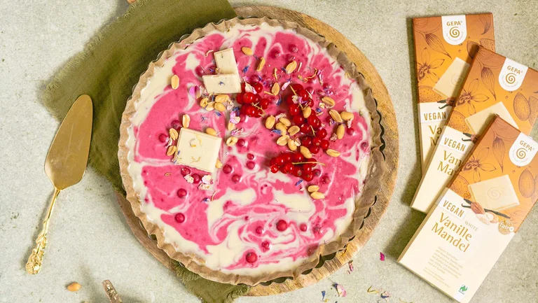 Weiß-pinke Tarte von oben. Daneben 3 Packungen helle GEPA-Schokolade