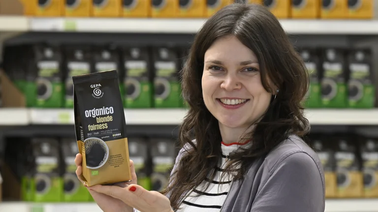 Sortimentsmanagerin Hanna Schmid mit Kaffeepackung "organico blonde fairness" in der Hand vor Regal mit weiteren Organico-Varianten.