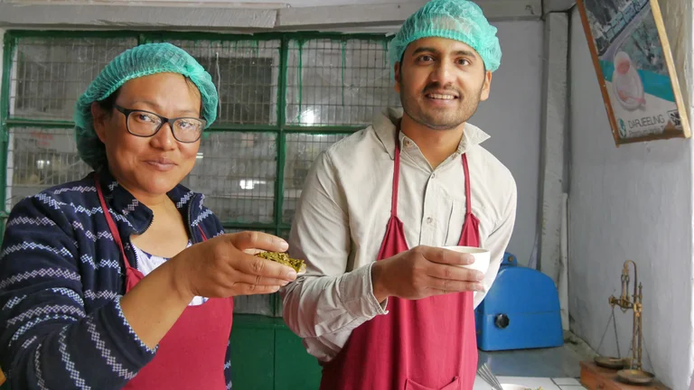 Bhawana Rai mit Gautam Mohan, beide tragen Haarnetze, sie haben Teeblätter und eine Teetasse in der Hand.