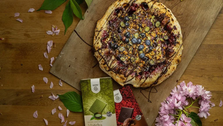 Pizza mit süßem schokoladigem Belag, daneben liegen zwei Tafeln GEPA-Schokolade