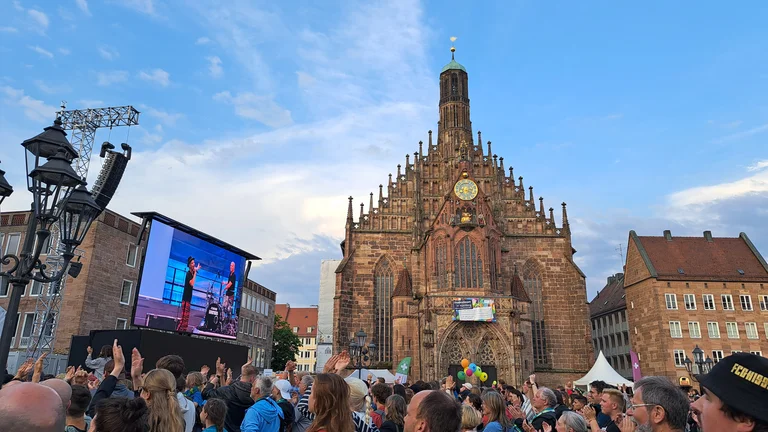 Blick auf die Frauenkirche in N&uuml;rnberg. Konzertbesucher verfolgen das Konzert von Brings auf einer Leinwand.