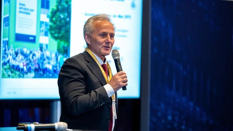 Matthias Kroth spricht ins Mikrofon, hinter ihm eine Pr&auml;sentation, die gerade das GEPA-Geb&auml;ude und das Mitarbeitenden-Foto zeigt. 