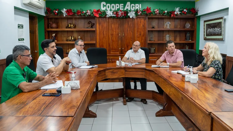 F&uuml;nf M&auml;nner und eine Frau sitzen sich an einem Konferenztisch gegen&uuml;ber und sprechen miteinander. Im Hintergrund an der Wand steht der Schriftzug "COOPEAGRI"