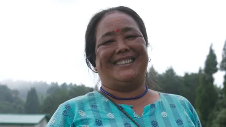 Portrait einer Frau mit Bindi. Sie lächelt in die Kamera. Im Hintergrund sind Bäume zu sehen.