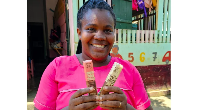 Frau vor einem Kindergartengebäude hält zwei GEPA-Schokoriegel in die Kamera