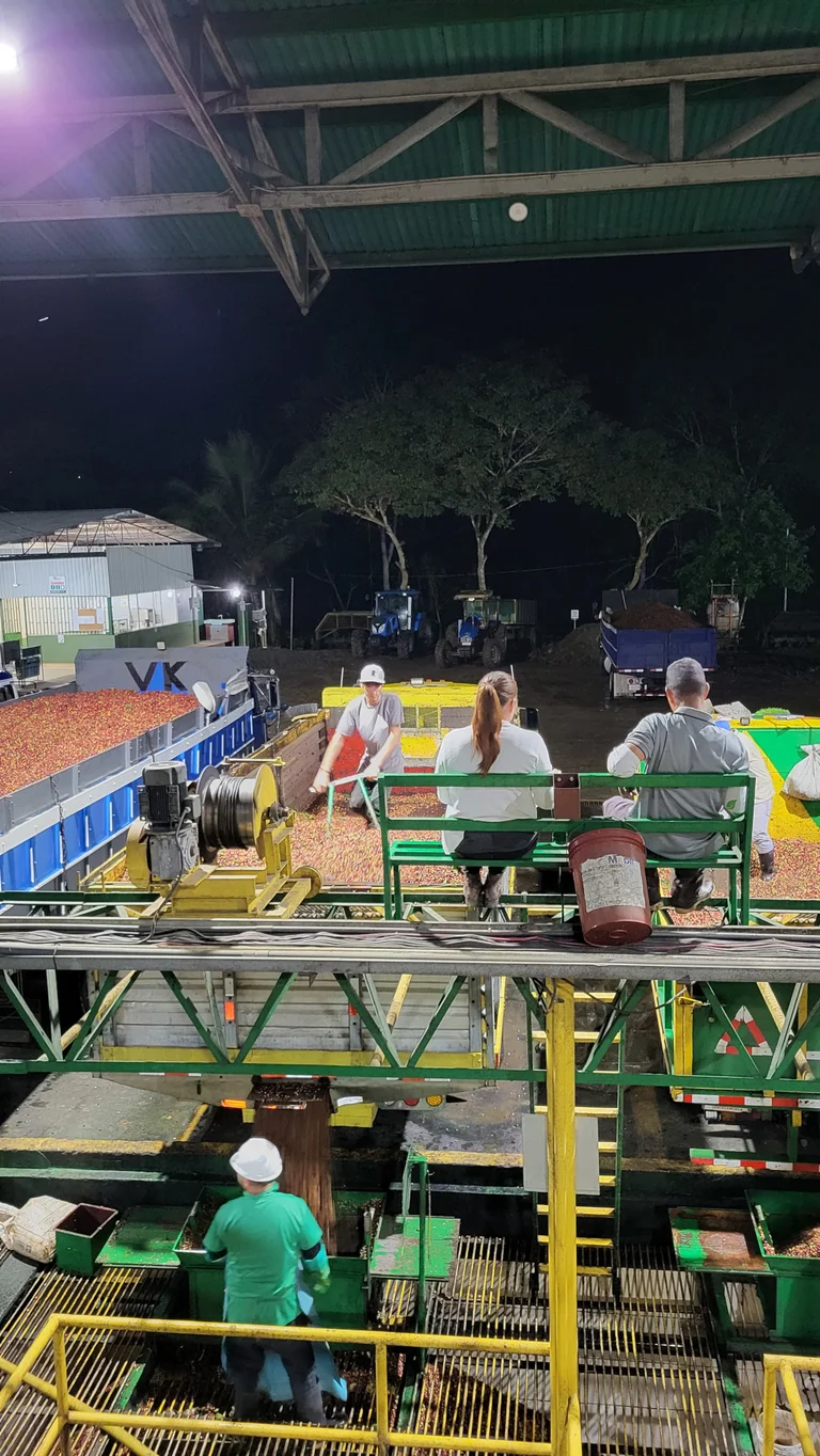 LKWs stehen an einer Verarbeitungsanlage f&uuml;r Kaffee. Mann und Frau sitzen oberhalb und &uuml;berwachen.