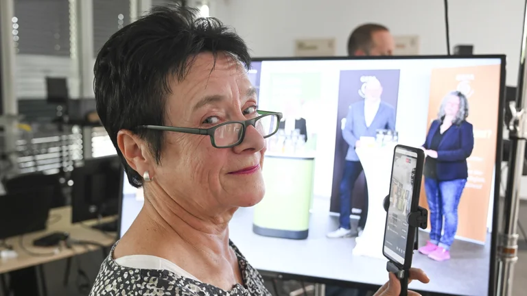 Portr&auml;t von Anne Welsing. Gerade streamt sie die Pressekonferenz live auf Instagram mit einem Smartphone. Im Hintergrund ein Bildschirm, der das Podium zeigt.