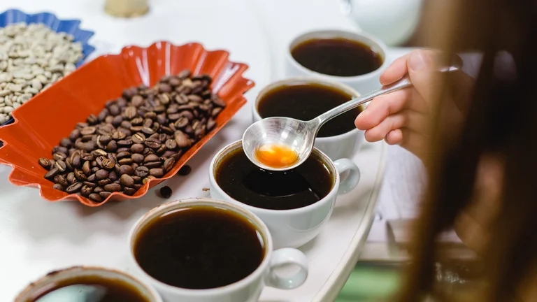 Nahaufnahme, wie ein runder, silberfarbener Löffel in den aufgebrühten Kaffee getaucht wird.