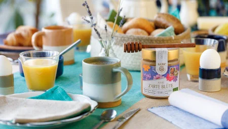 Blick &uuml;ber einen gedeckten Fr&uuml;hst&uuml;ckstisch u.a. mit Tassen, einem Br&ouml;tchenkorb, GEPA-Honig, Gl&auml;ser mit Orangensaft