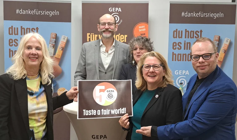 Gruppenbild von GEPA-Pressesprecherin Barbara Schimmelpfennig, GEPA-Geschäftsführer Peter Schaumberger, Bundesentwicklungsministerin Svenja Schulze und der Wuppertaler Bundestagsabgeordnete Helge Lindh. Sie halten ein Schild mit dem GEPA-Jubiläumslogo.