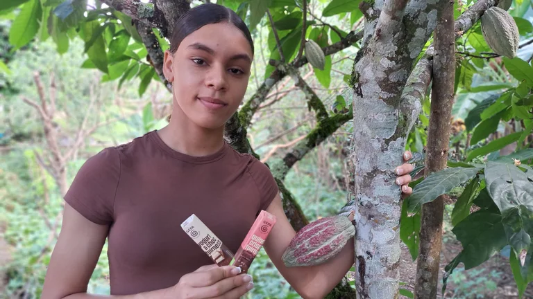 Teenagerin umfasst den Stamm eines Kakaobaums und hat zwei Schokoriegel in der Hand