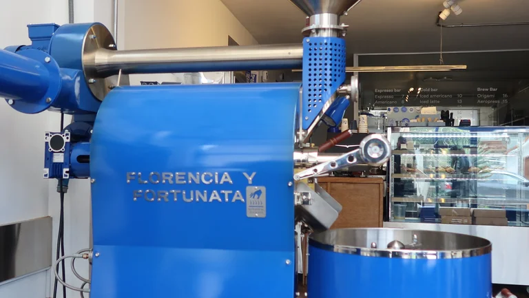 Nahaufnahme eines großen blauen Kaffeerösters, der in einem Café steht. Auf ihm die Aufschrift "Florencia y Fortunata"