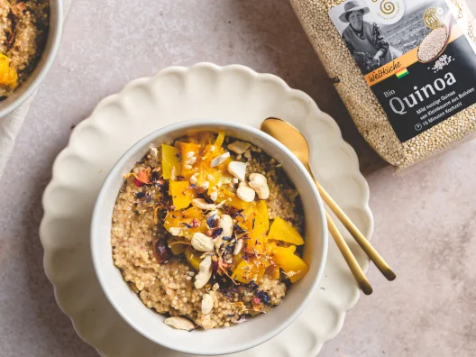 Quinoa-Porridge in einer Schale mit L&ouml;ffel auf einem Unterteller. Daneben eine Packung GEPA-Quinoa.