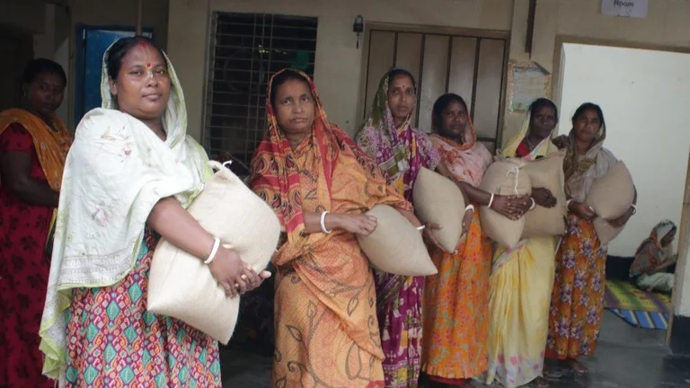 Sechs Frauen in Saris halten je einen Sack Reis und schauen in die Kamera