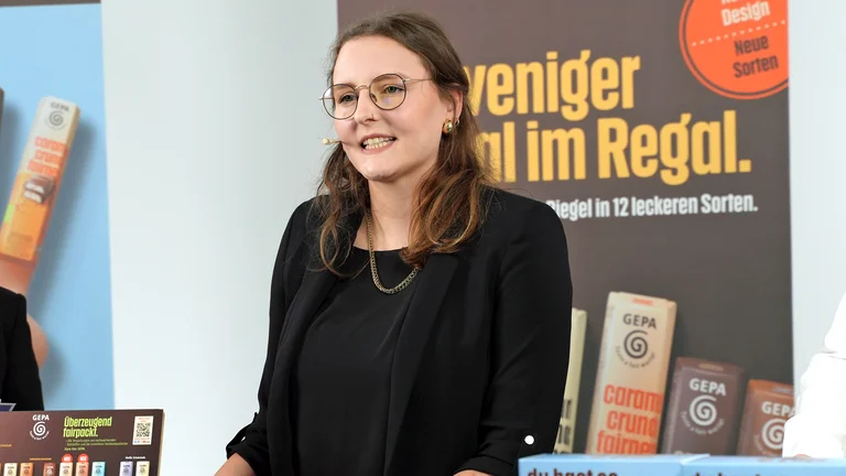 GEPA-Sortimentsmanagerin Alexandra Bleuel spricht in einem Studiosetting. Hinter ihr ein GEPA-Banner mit der Aufschrift "Für weniger egal im Regal"