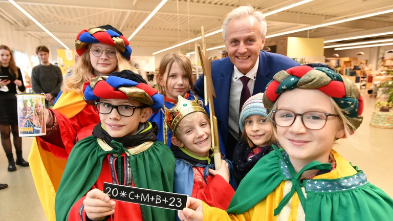 Sechs als Sternsinger verkleidete Kinder und GEPA-Geschäftsführer Matthias Kroth stehen im GEPA-Store und lächeln in die Kamera.