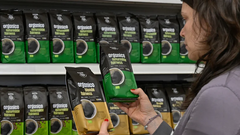 Die beiden Kaffeevarianten „organico blonde fairness” und „organico naturmilde fairness" werden von einer Person vor dem Organico-Regal in den Händen gehalten.
