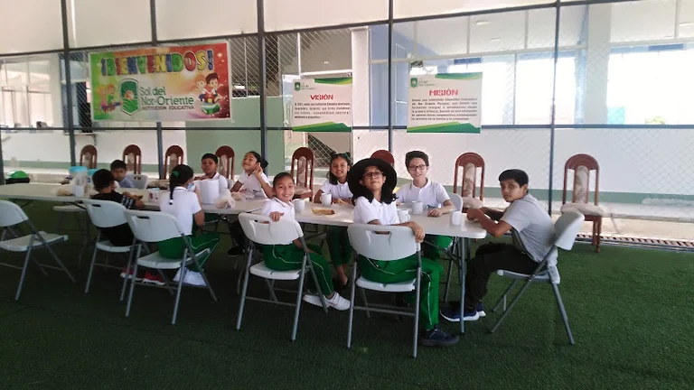 Gruppe von zehn Kindern, alle in wei&szlig;em Polohemd und gr&uuml;ner Hose, sitzen an einem langen Tisch.