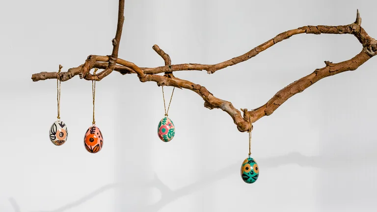 Von einem Zweig h&auml;ngen vier bunt bemalte Eier jeweils an einer Kordel.