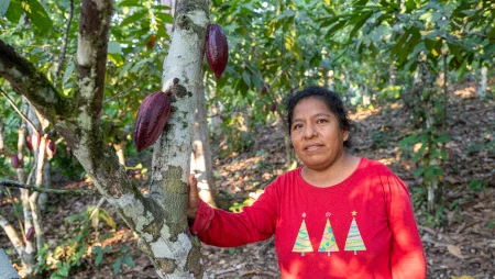 Eine Kakaobäuerin steht an einem Kakaobaum im Wald