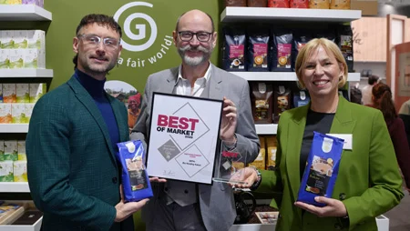 Zwei M&auml;nner und eine Frau auf der Messe INTERNORGA: Der Mann in der Mitte h&auml;lt eine Urkunde mit "Best of Market" in die Kamera. Die anderen beiden halten je eine Packung Kaffee in H&auml;nden.