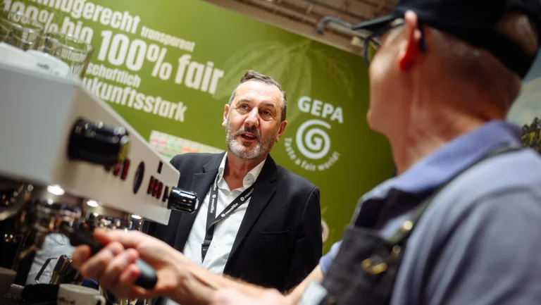 Mann unterh&auml;lt sich mit einem Barista an einer Siebtr&auml;germaschine.