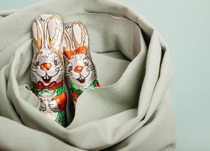 Zwei verpackte Schokoladenhasen schauen aus einem Tuch, in das sie eingewickelt sind.