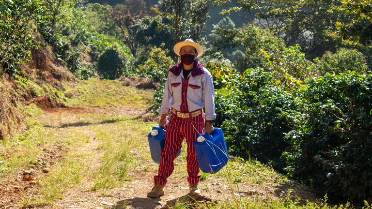 Mann auf einem Feldweg trägt Kanister in seinen Händen