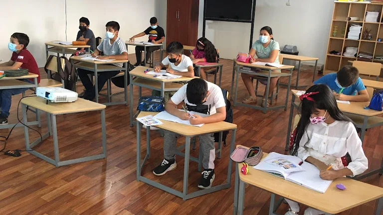 Sch&uuml;ler*innen in einem Klassenzimmer, alle an einem kleinen Einzeltisch. Sie trafen Atemschutzmasken.