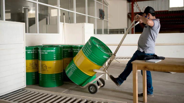 Ein Man stellt per Sackkarre ein Fass zu anderen Fässern