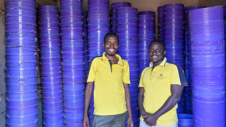 Zwei Männer in gelben Polohemden stehen vor Stapeln von blauen Eimern