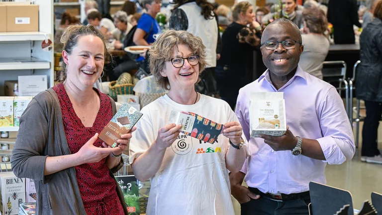 Zwei Frauen und ein Mann unterschiedlicher Hautfarbe mit GEPA-Produkten in der Hand und fröhlich guckend.