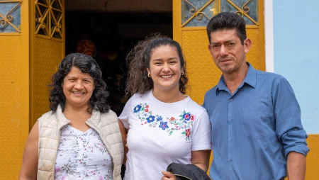 Vor einem Hauseingang stehen eine Frau, eine junge Frau und ein Mann eng nebeneinander und lächeln in die Kamera.