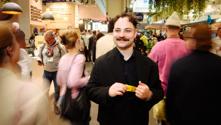 Junger Mann l&auml;uft durch eine Messehalle und hat einen GEPA-Nussriegel in der Hand. Um ihn herum verschwommen die Menschenmenge.