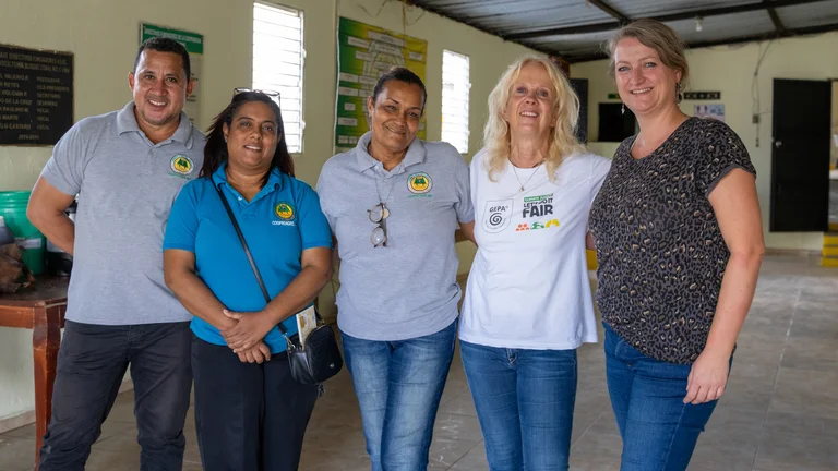 Vier Frauen und ein Mann in einem großen Raum haben die Arme um die Schultern gelegt und lächeln in die Kamera.