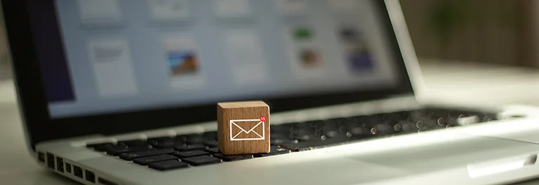 Auf der Tastatur eines Laptops liegt ein Holzw&uuml;rfel mit einem wei&szlig;en Briefsymbol darauf