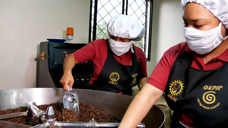 Zwei Frauen mit Haarnetzen und Mundschutz arbeiten an der Rösttrommel.
