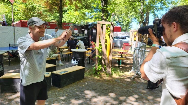 Jojo Gerner von Querbeat in einem Backstage-Bereich auf einem Festivalgel&auml;nde. Jemand filmt ihn. Er h&auml;lt einen GEPA-Schokoriegel in dessen Kamera.