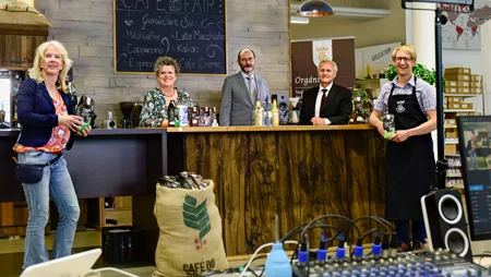 Zwei Frauen und drei M&auml;nner stehen vor bzw. hinter einer Kaffeetheke. Sie l&auml;cheln in die Kamera. Im Vordergrund sind Mischpulte und weitere Technik aufgebaut.